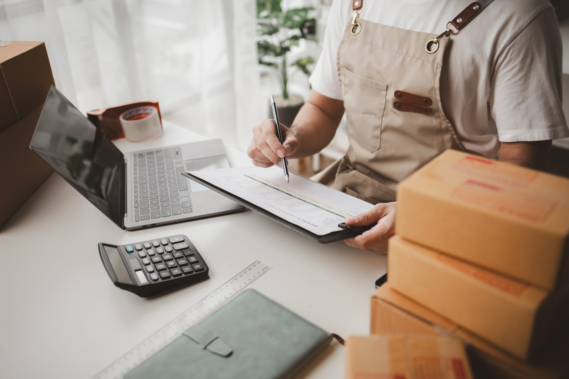 Workspace with shipping boxes, laptop, calculator, and order form, representing ecommerce support for church online stores.
